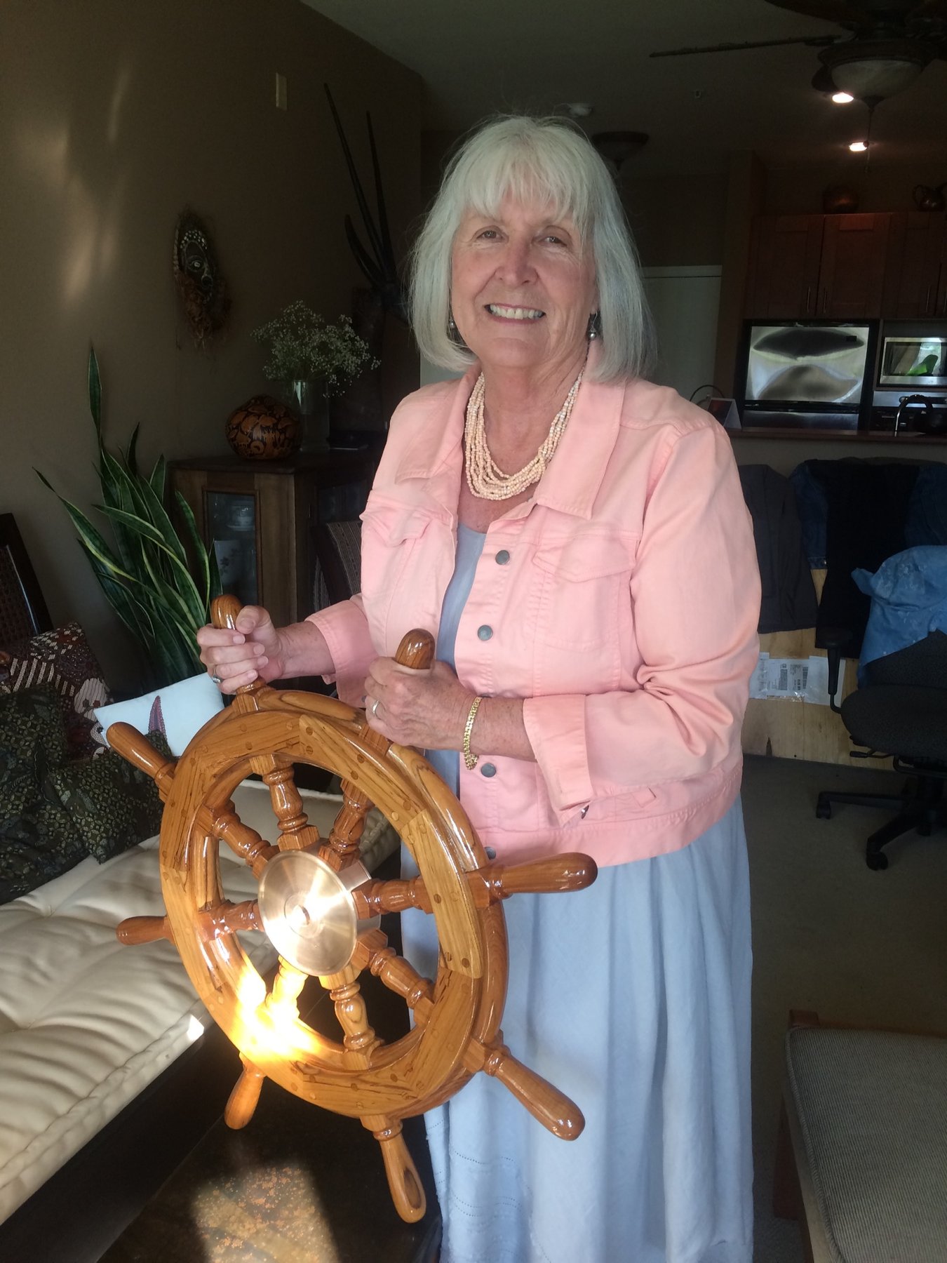 A smiling crew member proudly displays the beautifully restored wooden ship's wheel of the classic 1946 Philip Rhodes-designed Merry Maiden, docked in Puget Sound.