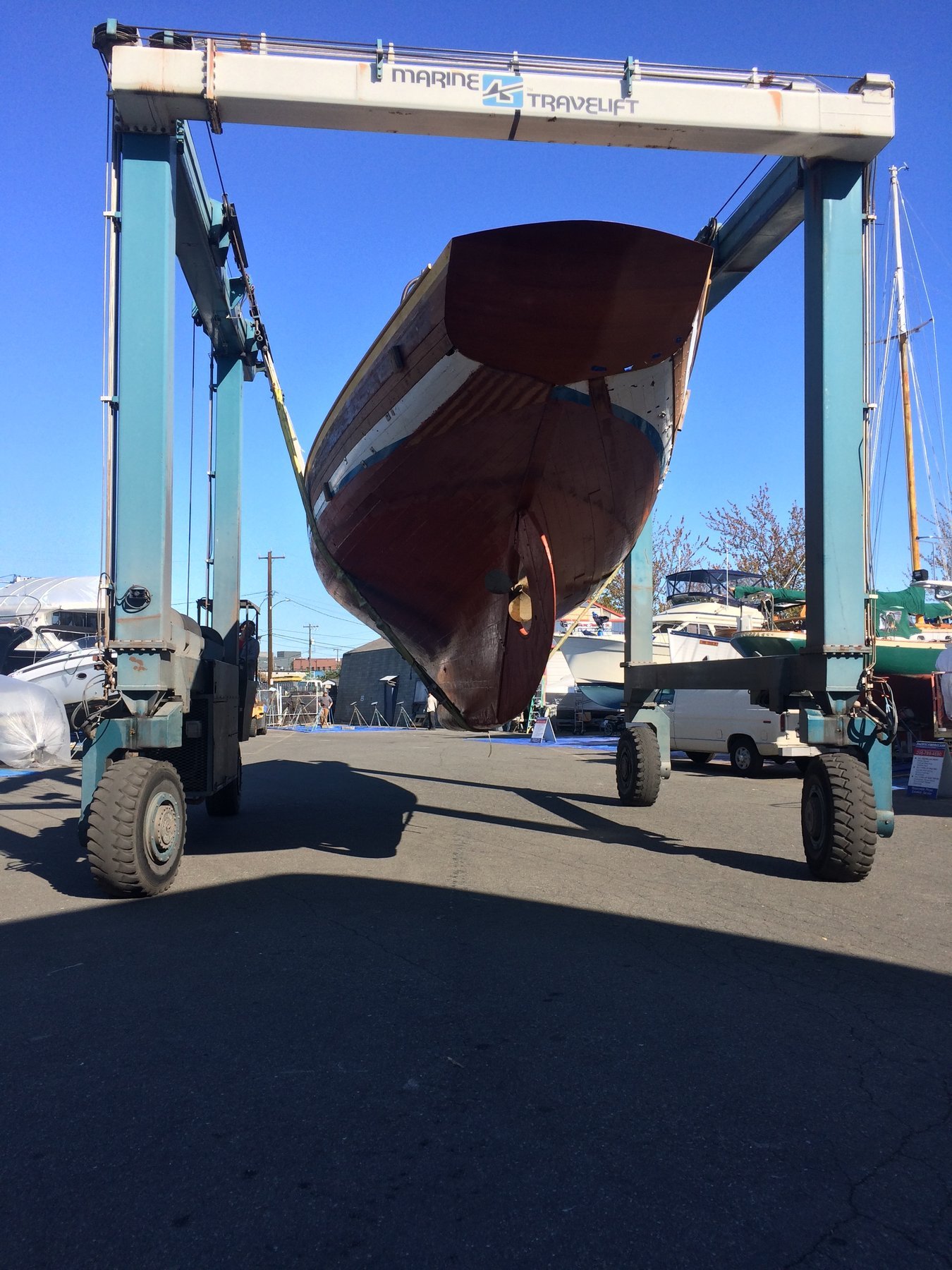 The classic Merry Maiden, a 1946 Philip Rhodes design, rests in the boatyard under brilliant blue skies, her mahogany hull gleaming as she awaits restoration or maintenance in the Pacific Northwest.