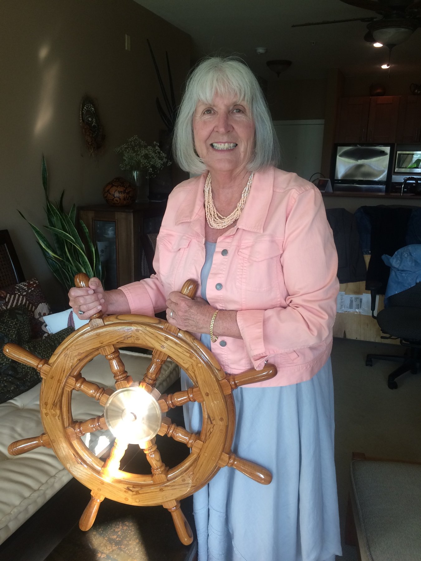 A beaming crew member poses with the ship's wheel of the classic 1946 Philip Rhodes-designed Merry Maiden, her hands confidently gripping the wooden helm that has guided this 35-foot yacht through decades of sailing.