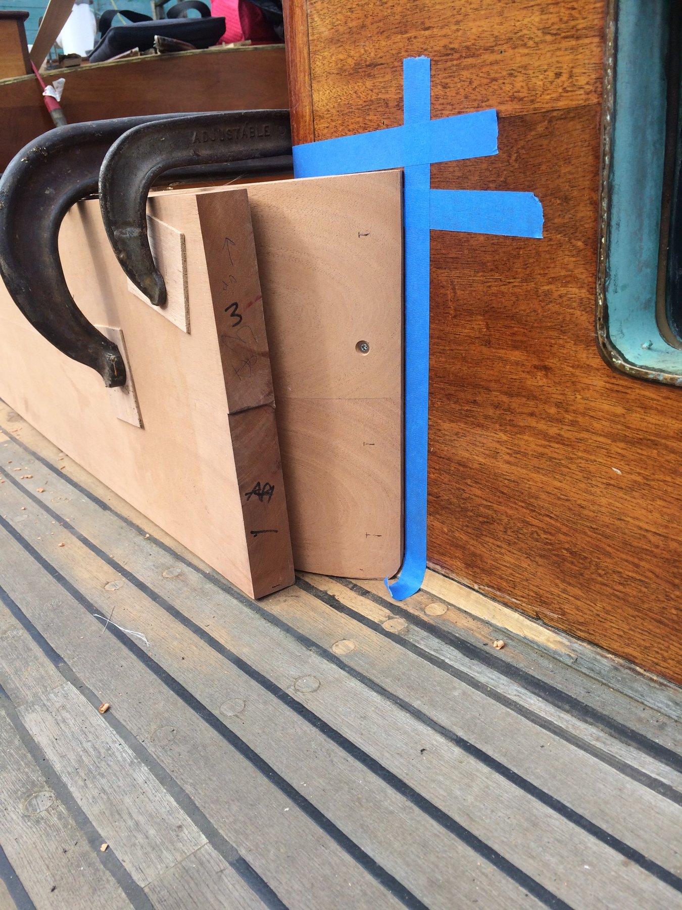 Restoration work on the classic 1946 Philip Rhodes-designed Merry Maiden, with blue painter's tape marking the deck and a wooden batten positioned for measurement, revealing the meticulous craftsmanship required to preserve this vintage wooden yacht.