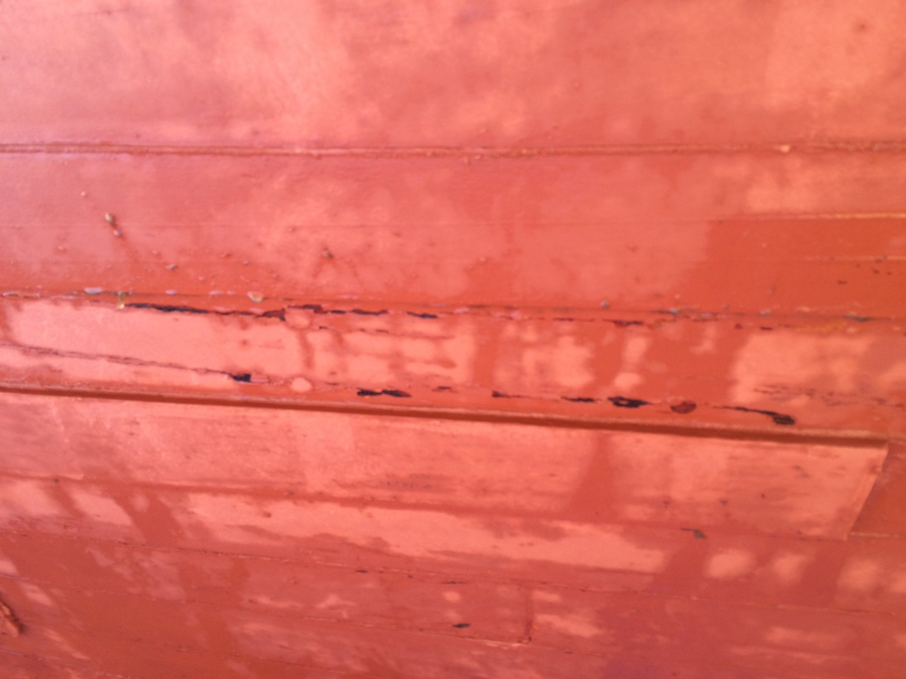 The weathered hull of the classic 1946 Philip Rhodes-designed Merry Maiden displays the patina of decades, with peeling paint and dark streaks revealing the wooden planking beneath—a testament to this vintage Puget Sound cruiser's storied history.