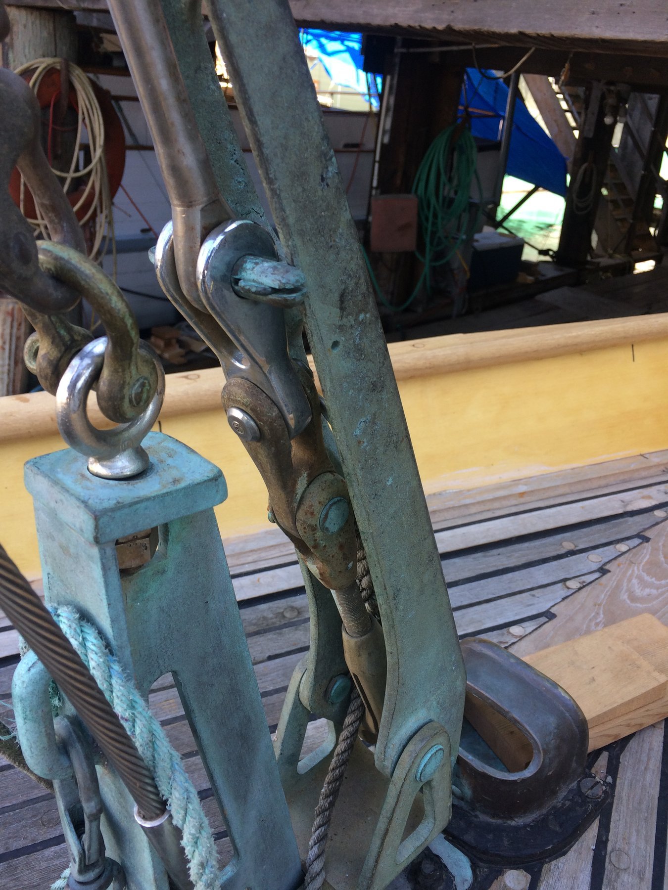 Weathered bronze blocks and tackle on the Merry Maiden's boom, showing the patina of a classic 1946 yacht's working rigging and the craftsmanship of mid-century yacht design.