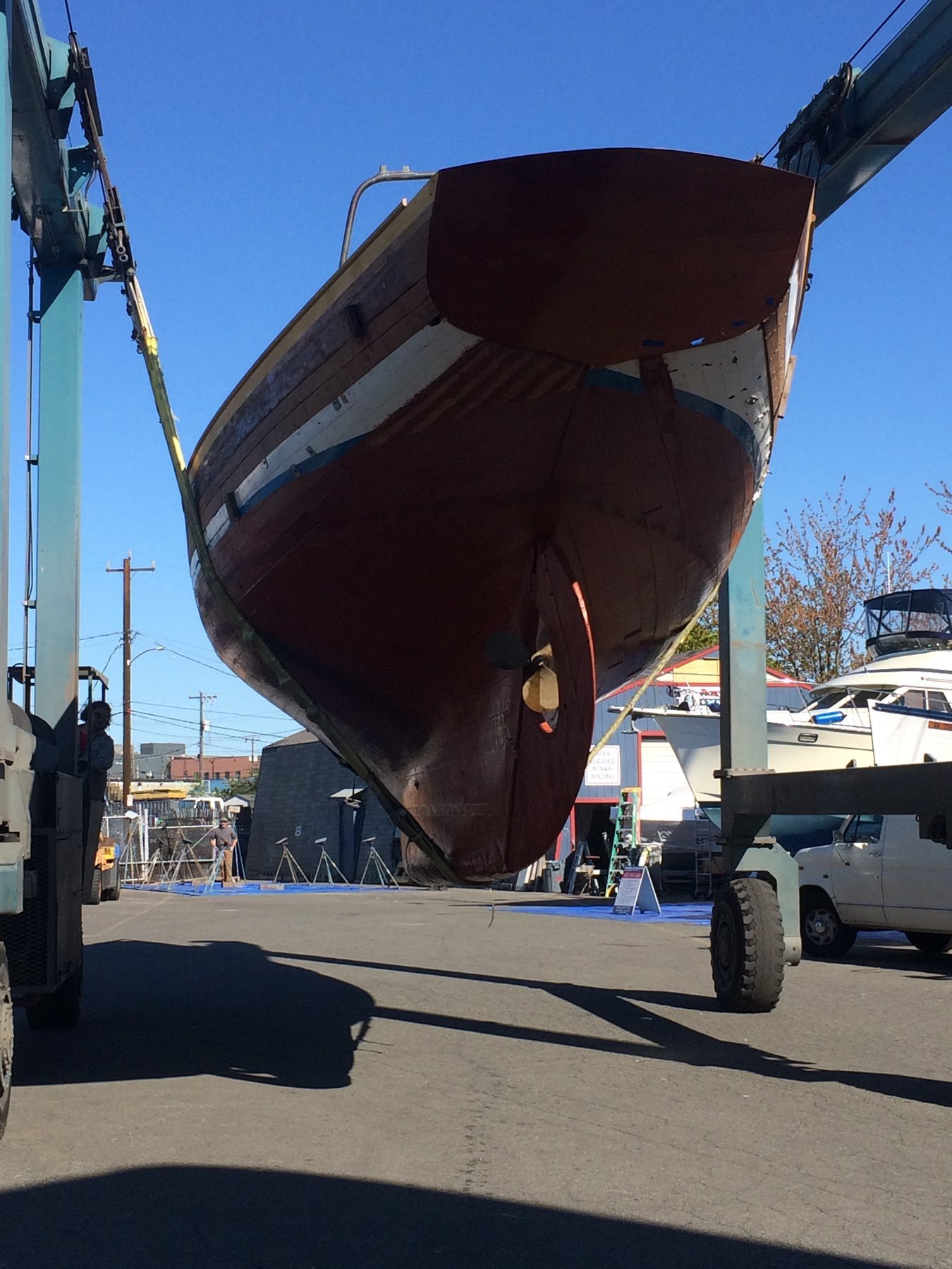 The classic 1946 Philip Rhodes-designed Merry Maiden rests in the Puget Sound boatyard, her dark hull and graceful lines silhouetted against a crystalline spring sky.