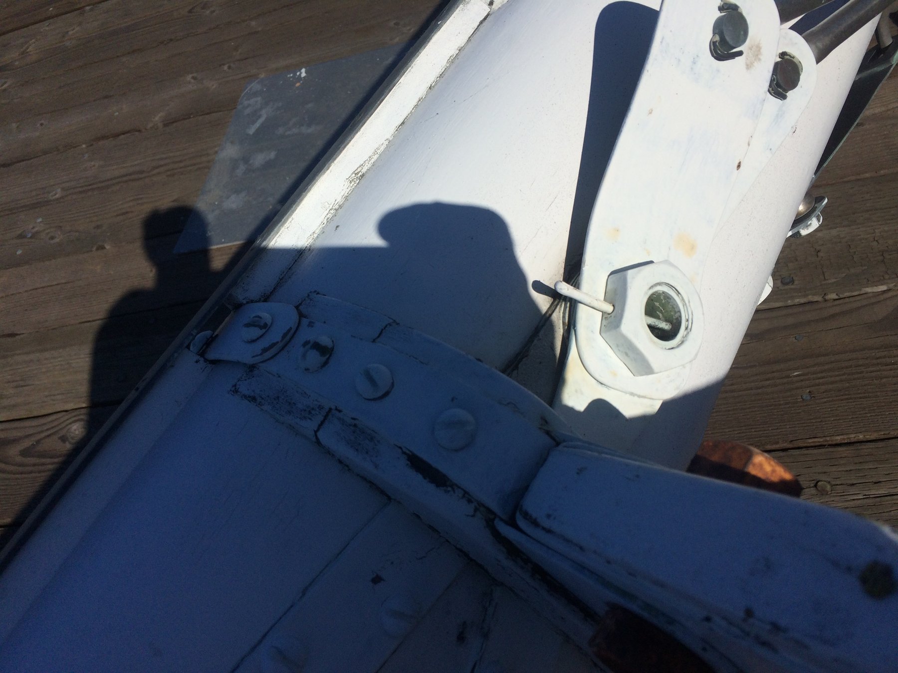 Sunlit detail of the Merry Maiden's white cabin trunk and deck hardware, with the photographer's shadow cast across the classic 1946 yacht's navy hull at rest on Puget Sound.