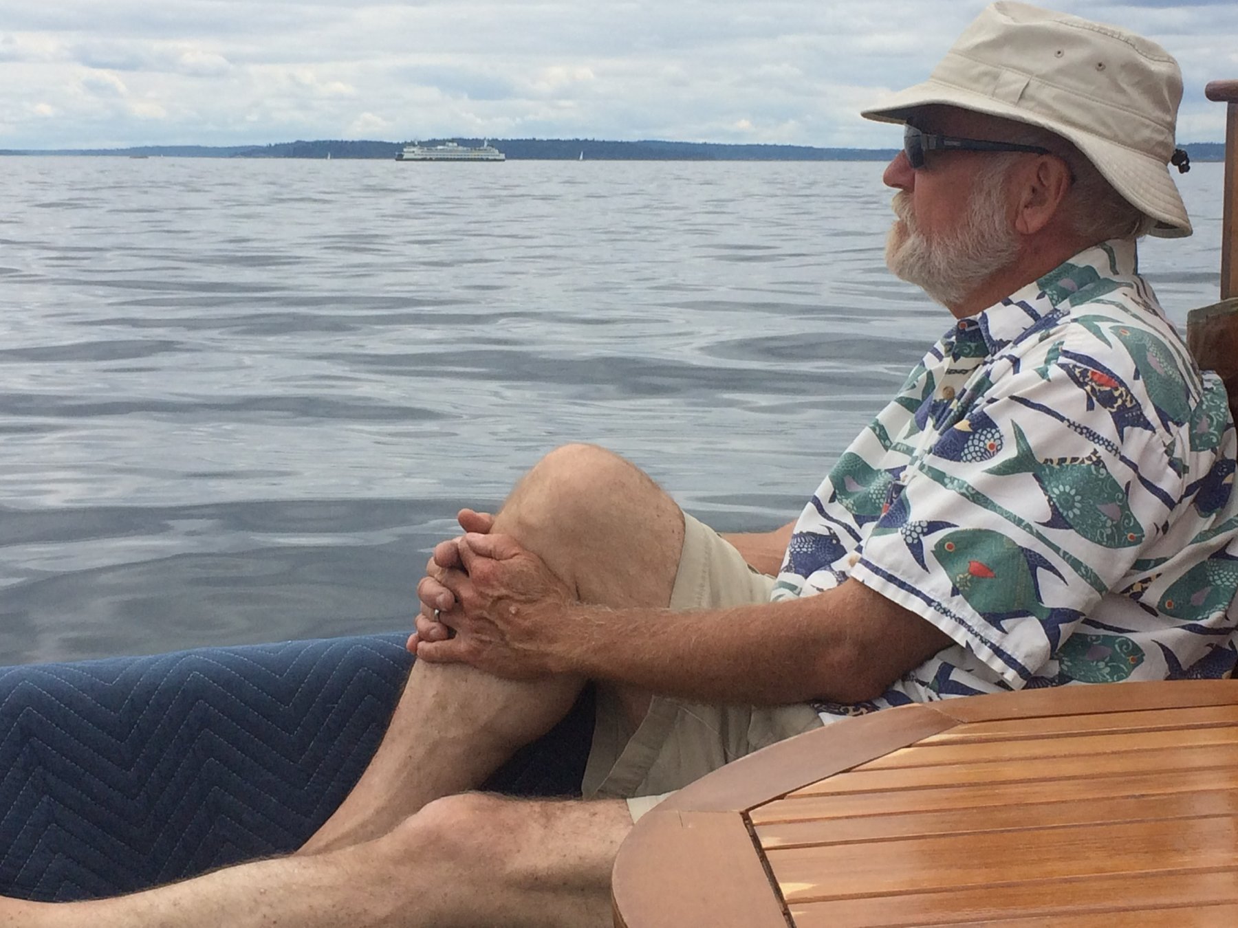 A relaxed moment aboard the classic 1946 Merry Maiden, anchored in the calm waters of Puget Sound with distant ferries and forested shores completing the Pacific Northwest scene.