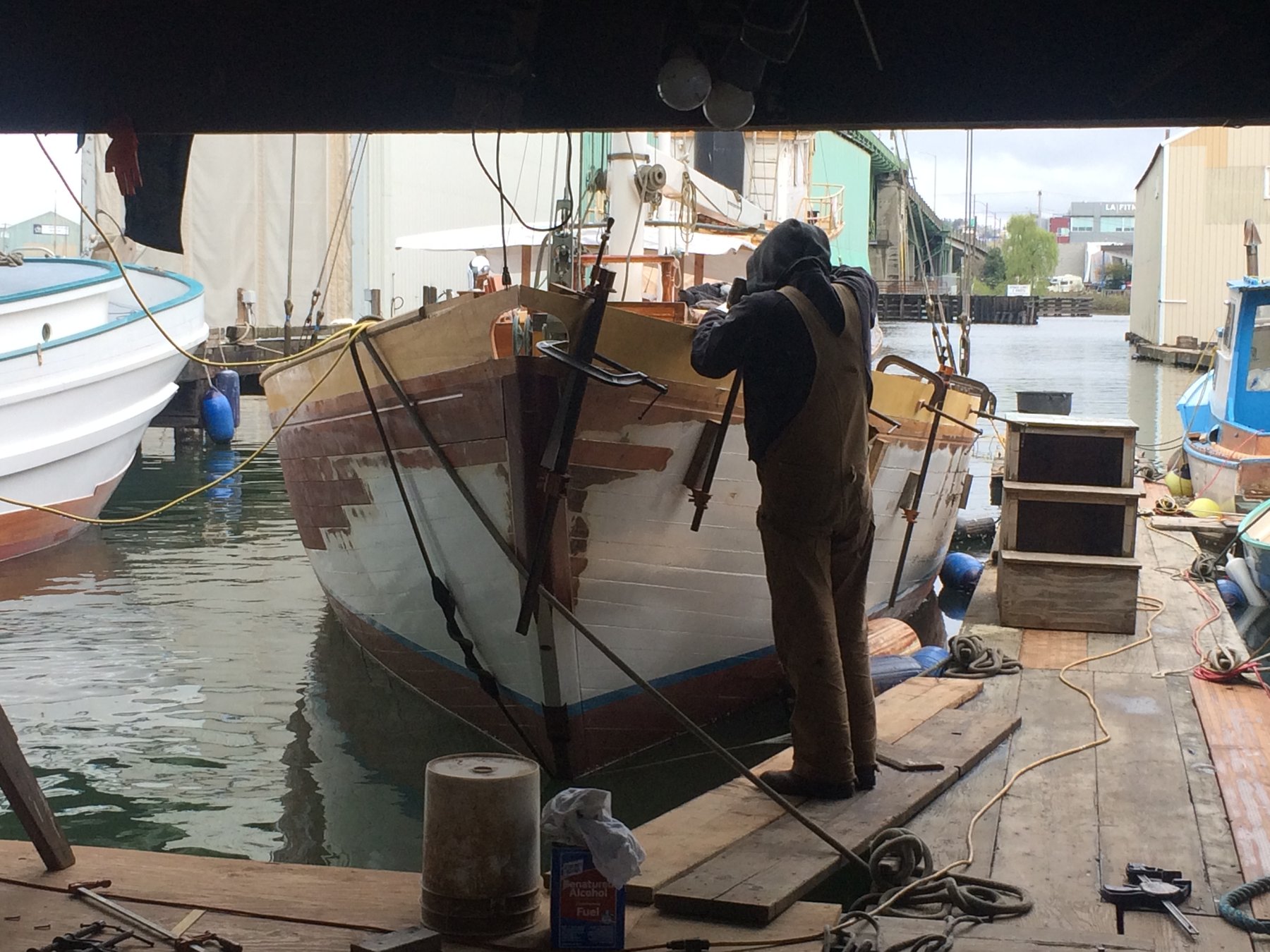A worker tends to the classic lines of Merry Maiden, the 1946 Philip Rhodes-designed yacht, during maintenance at a Puget Sound shipyard, her graceful hull reflecting decades of Pacific Northwest sailing heritage.