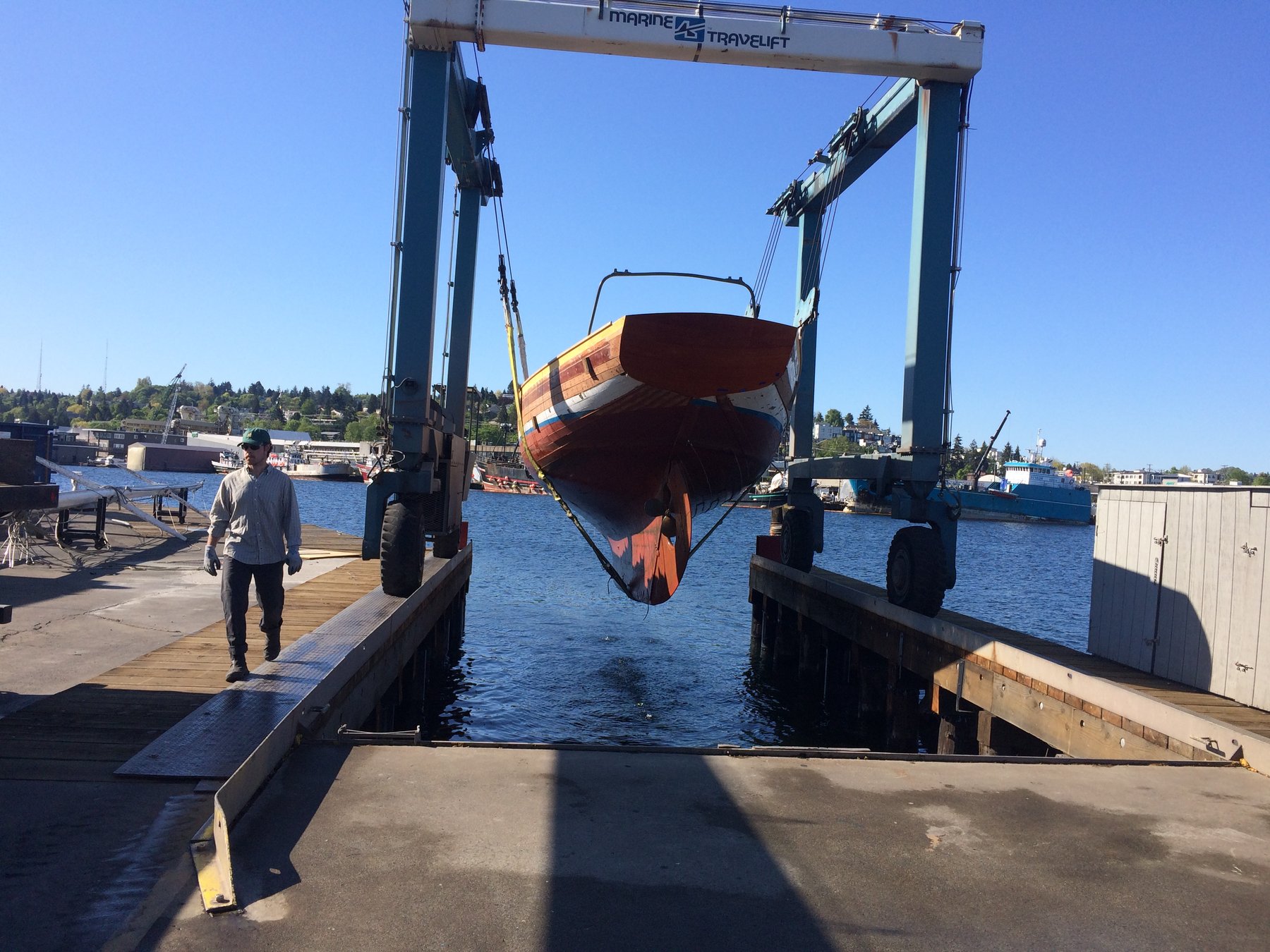 The classic 1946 Philip Rhodes-designed Merry Maiden suspended in the Marine Travelift at a Puget Sound boatyard, her wooden hull gleaming as she's carefully hoisted for maintenance and restoration work.