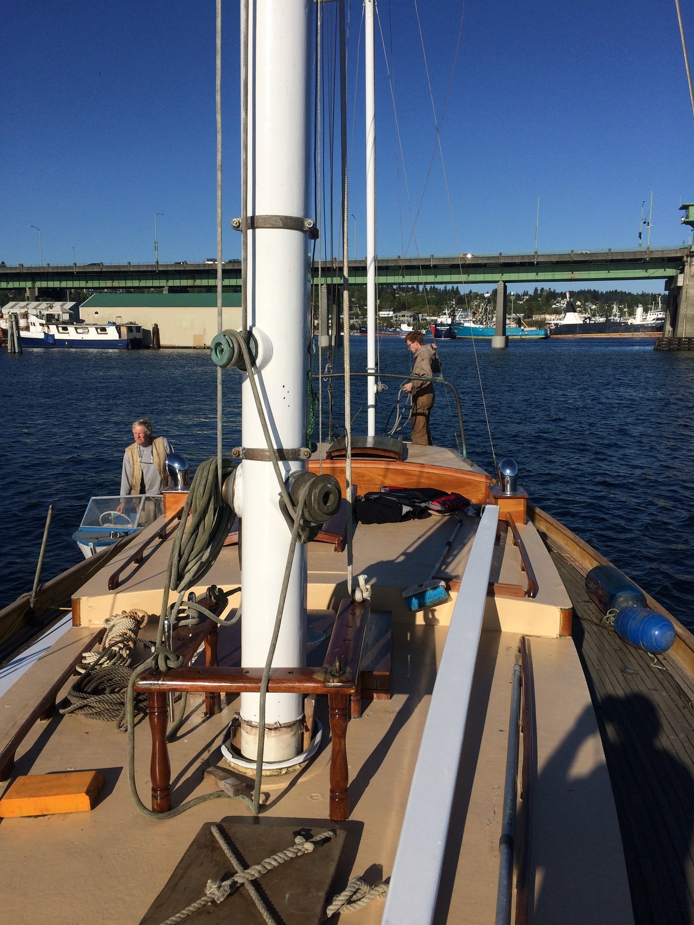 The classic lines of Merry Maiden's boom and rigging frame a sunny day on Puget Sound, with the 1946 Philip Rhodes design moored peacefully against the clear blue water and distant shoreline.
