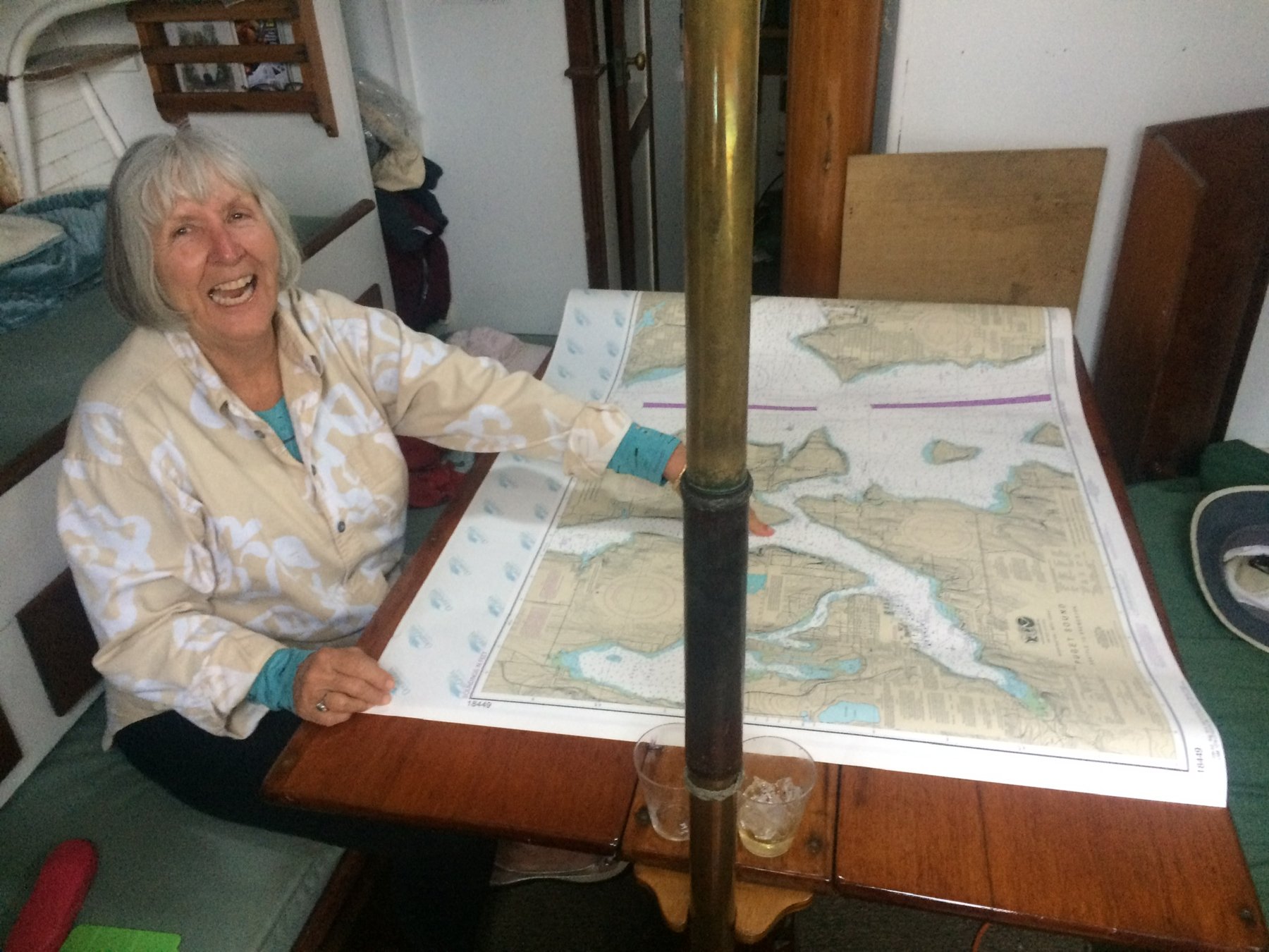 Candace studies navigation charts aboard the classic 1946 Philip Rhodes-designed Merry Maiden, anchored in Washington's Puget Sound with brass instruments gleaming in the cabin light.