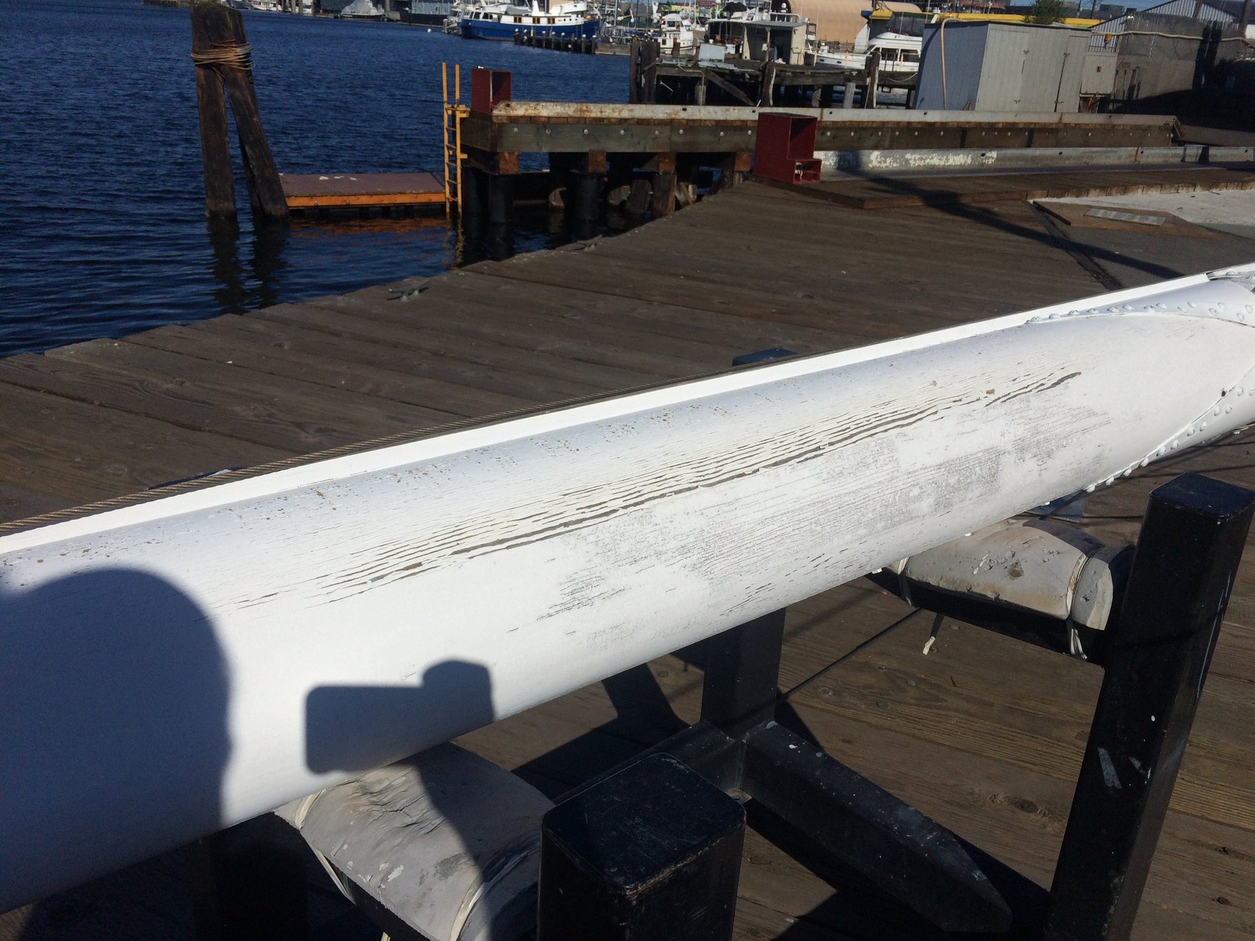A classic 1946 Philip Rhodes-designed mast rests on wooden supports at a Puget Sound boatyard, its weathered white surface telling stories of decades at sea.