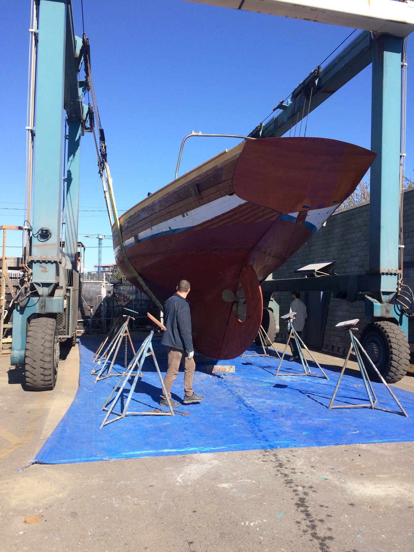 The classic 1946 Philip Rhodes-designed Merry Maiden rests on the hard under brilliant Puget Sound skies, her burgundy hull gleaming against the blue work platform as restoration work continues.