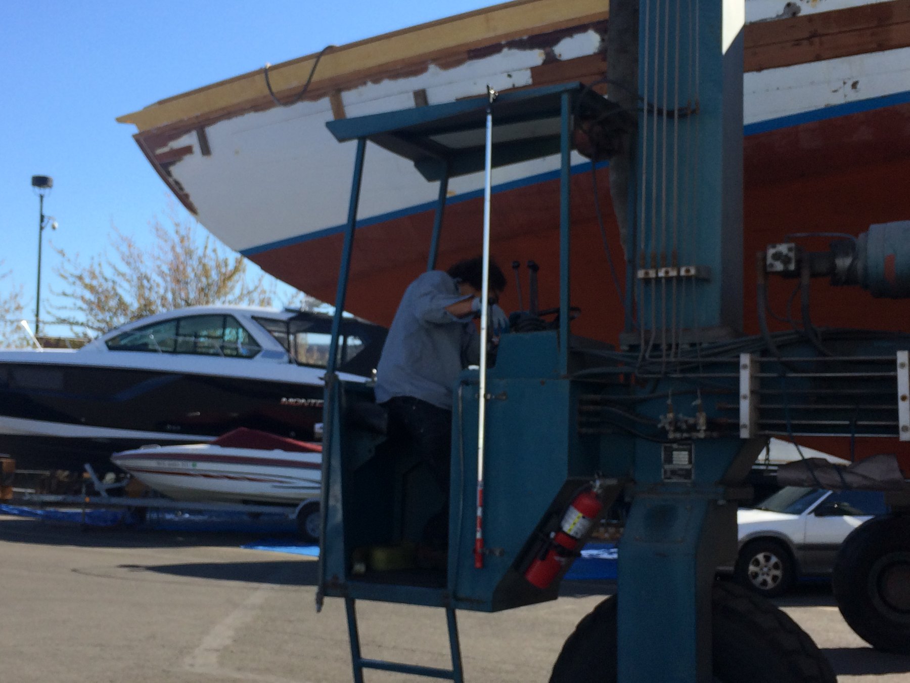 A worker tends to the classic 1946 Philip Rhodes yacht Merry Maiden during haul-out at a Puget Sound boatyard, with her distinctive red hull and white topsides gleaming in the spring sunshine.