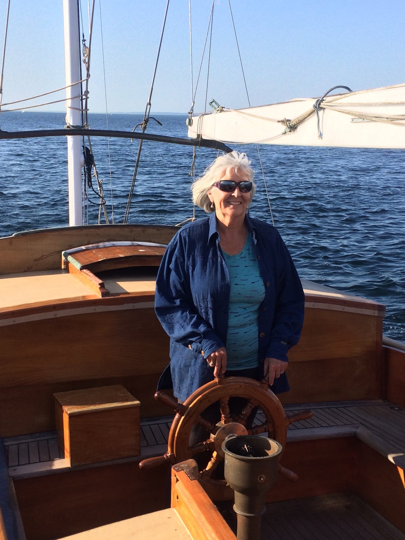 At the helm of the classic 1946 Merry Maiden, a Philip Rhodes design, the skipper steers through calm Puget Sound waters with traditional wooden wheel and pristine canvas aloft.