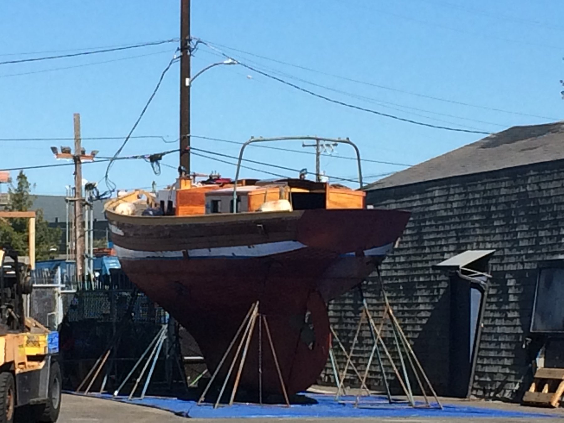 The classic 1946 Philip Rhodes-designed Merry Maiden sits cradled in the boatyard, her mahogany and cream hull suspended on wooden shores under the clear Puget Sound sky, awaiting restoration or maintenance.
