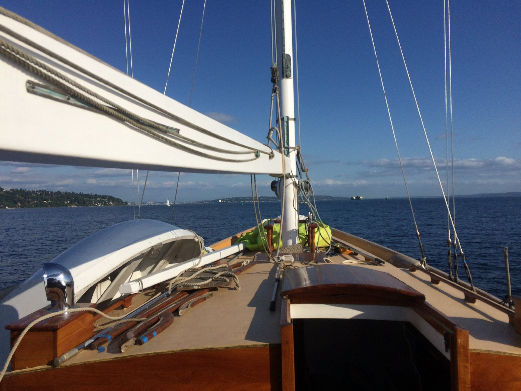 The classic lines of Merry Maiden's deck stretch toward Puget Sound's calm waters, her white sails and wooden trim gleaming under brilliant blue skies as she glides past the forested shores of the Pacific Northwest.