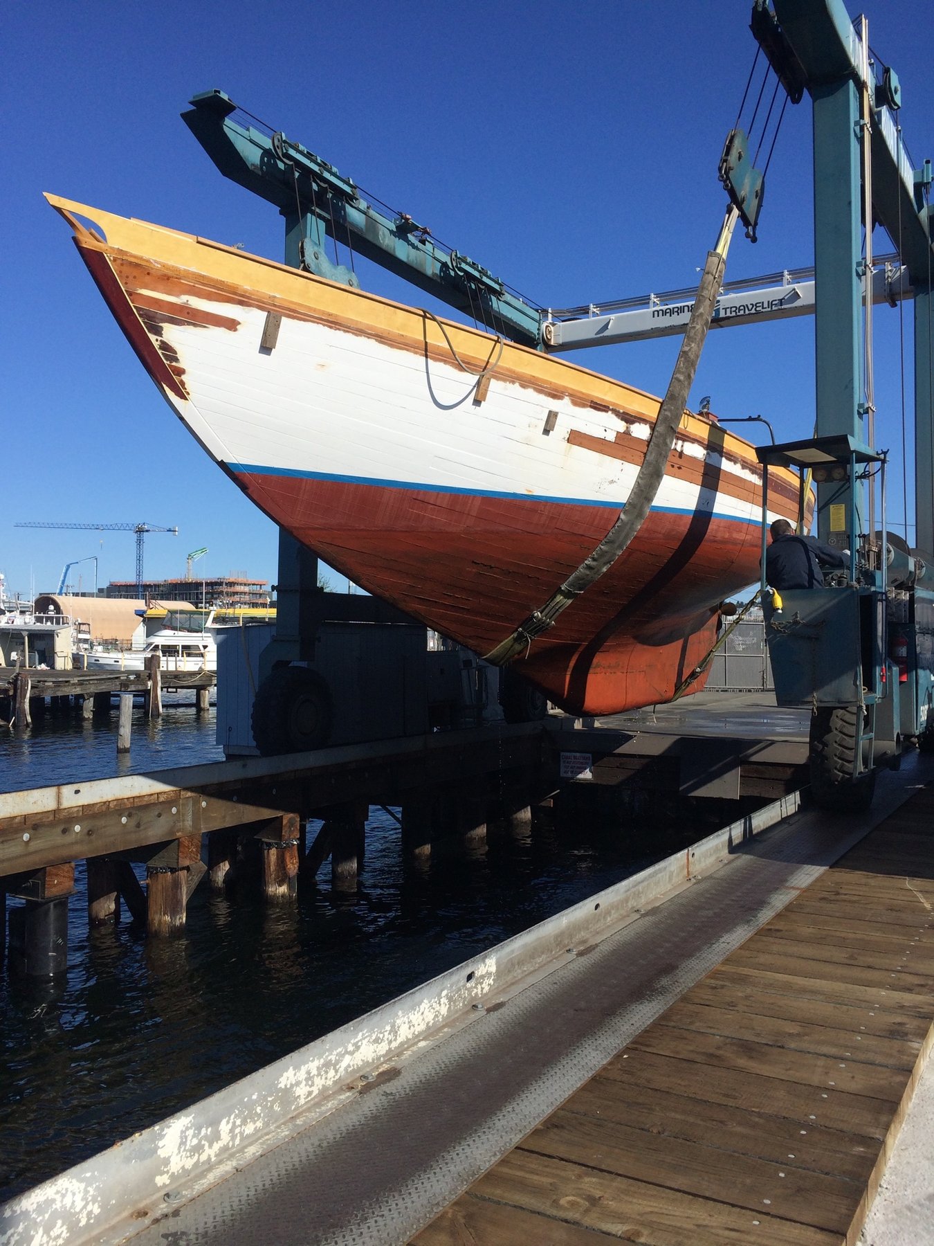 The beautifully restored Merry Maiden, a 1946 Philip Rhodes classic, hangs suspended in the boat lift at the marina, her gleaming yellow topsides and traditional red hull a testament to meticulous preservation.