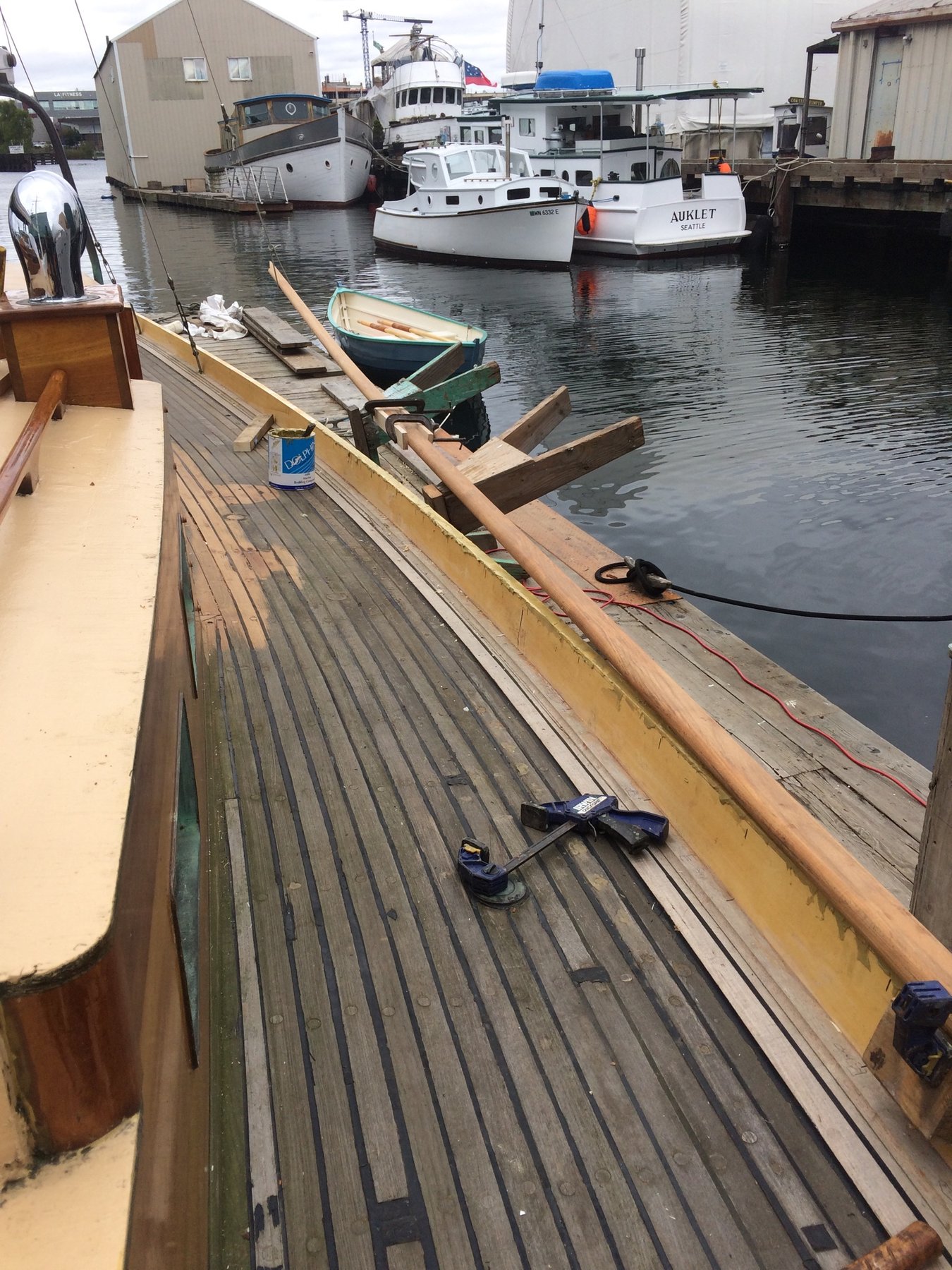 The Merry Maiden rests peacefully at her moorings in a working harbor, her wooden deck and traditional rigging showcasing the timeless elegance of this 1946 classic design amid the working fishing boats and maritime infrastructure of the Pacific Northwest.