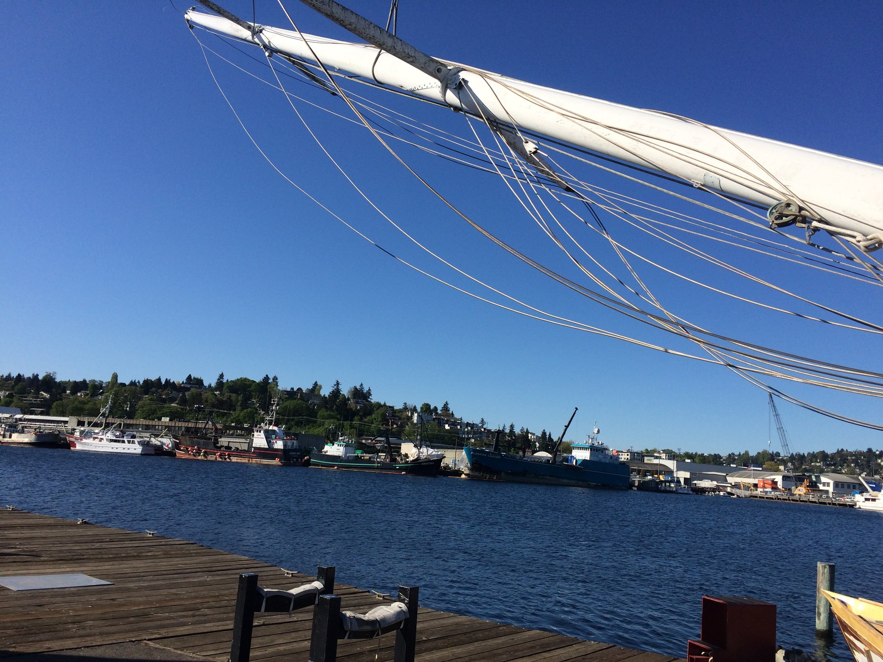 The classic lines of Merry Maiden's rigging frame a bustling Puget Sound maritime scene, where working vessels and waterfront infrastructure reflect the region's rich nautical heritage under clear skies.